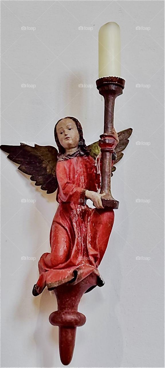 A gold winged angel in red holding a large white candle at “St. Katharinenkirche” or “St. Katharine’s” church in “Regensburg”, Germany shows the intricate artistry that goes into the making of this Karolingian inspired art. 2023. Hypnotic Productions