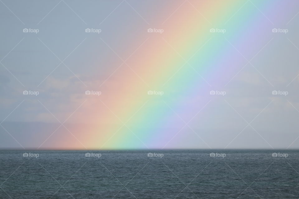 Bright rainbow closeup over ocean horizon on stormy day