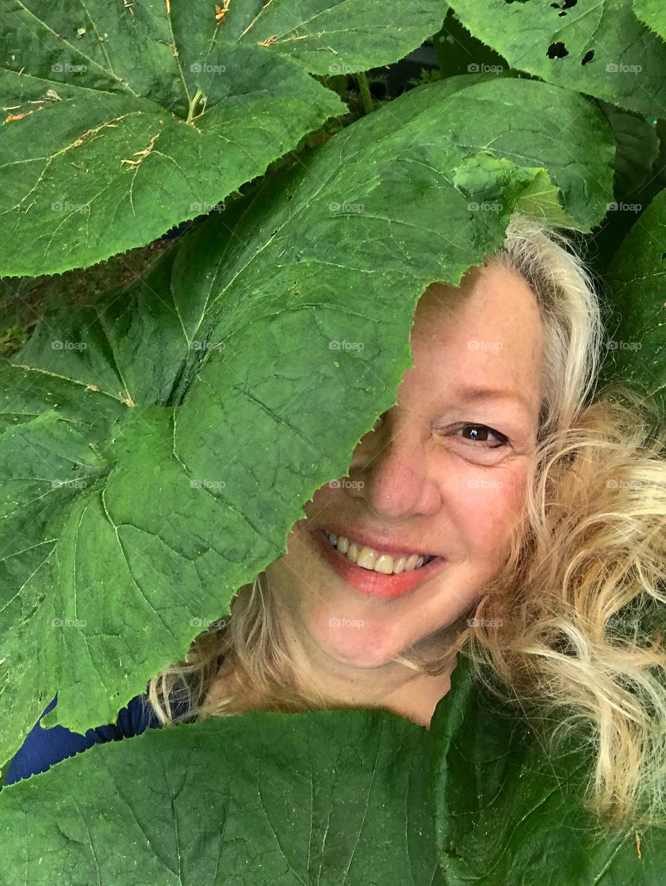 Self portrait of a smiling happy woman lying down amidst the umbrella plant leaves in her jungle garden. 