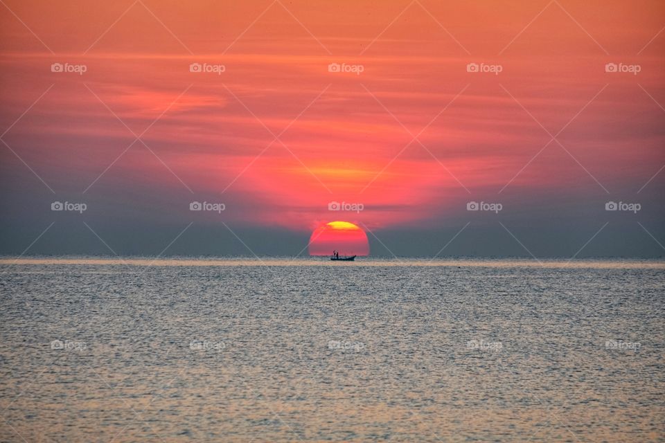 Background photo of a boat in the center of sunrise from the sea