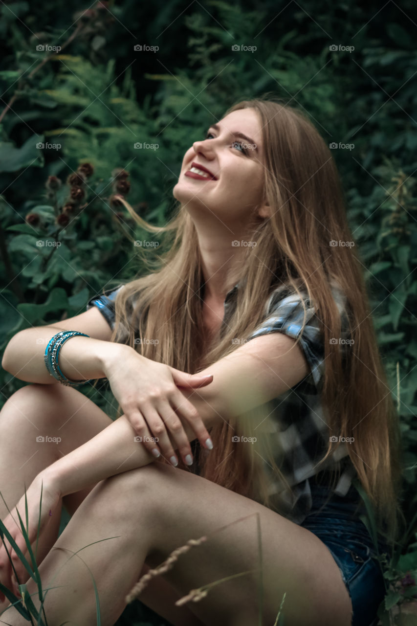 A girl with blond hair in a plaid shirt and short denim shorts on a background of trees and nature Girl, woman, man, people, blonde, blonde hair, checkered shirt, shorts shorts, denim shorts, forest nature, trees, grass, feelings, emotions tenderness, love, lifestyle, lifestyle, recreation
