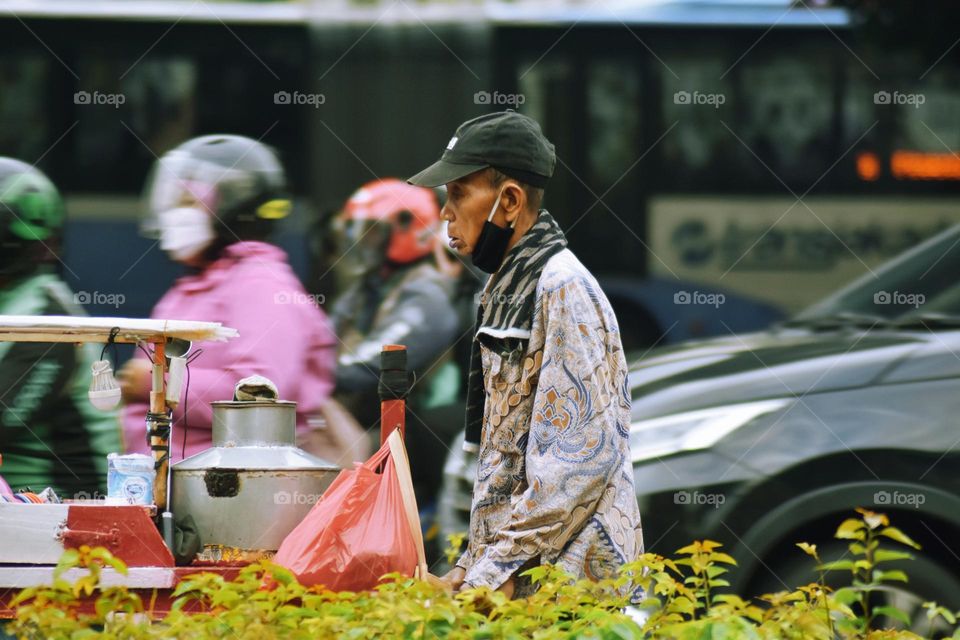 an old man pushing his cart on a street in Jakarta