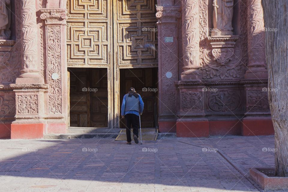 A man with cane is entering the doorway of a church in San Miguel de Allende, Mexico 
