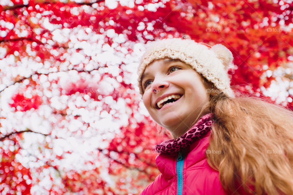 Low angle shot of happy girl under red blurred autumn tree