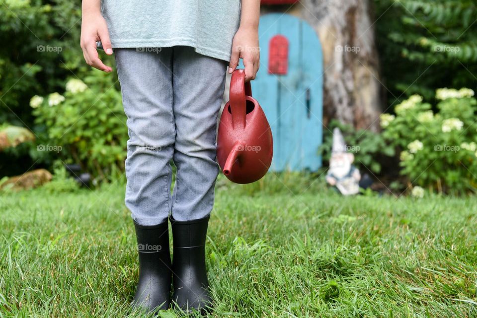 Young child holding a watering can in front of a little gnome house in an enchanted forest 