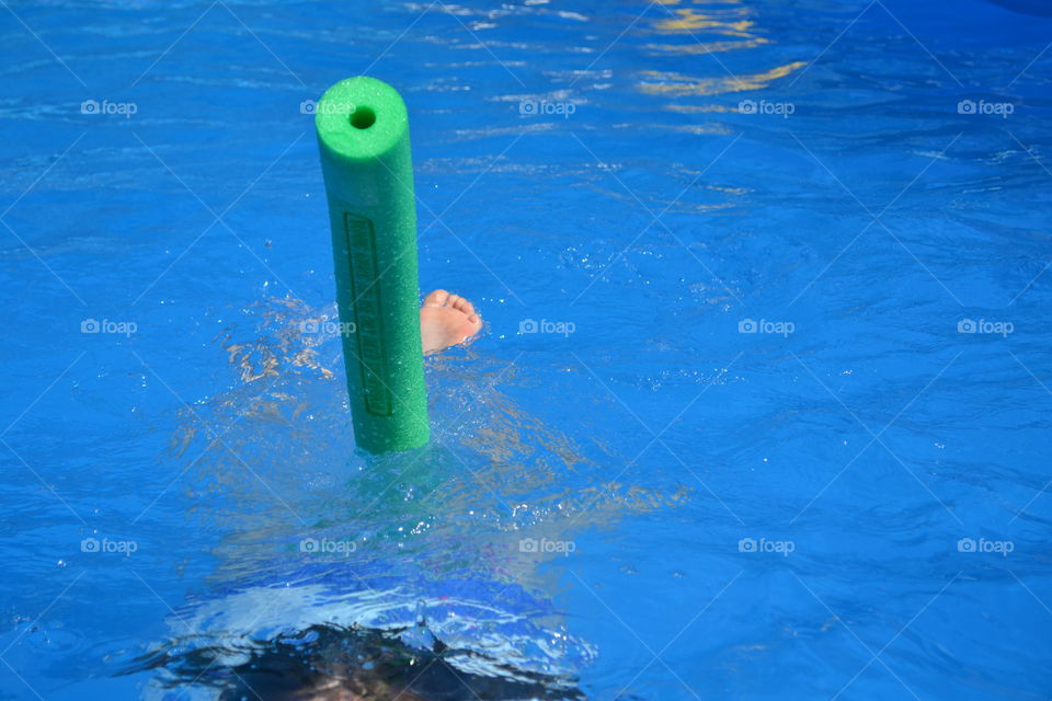 Green swimming pool noodle toy in swimming pool