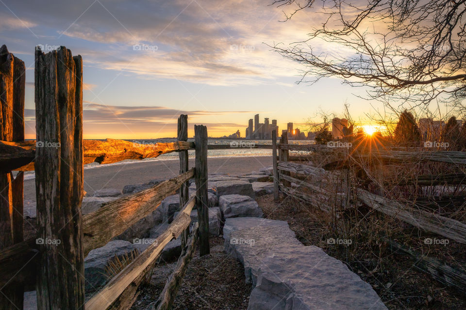 Stone path leading a beach and skyline past a wooden fence being illuminated with golden sunset light. 