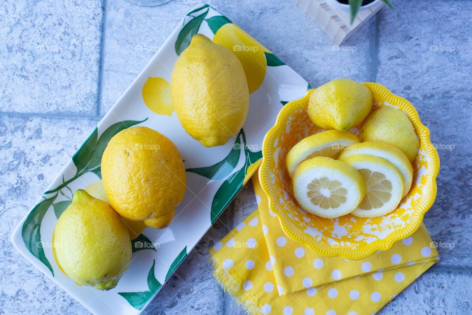 Top view of brightly colored yellow lemons on a colorful plate with a tile countertop 
