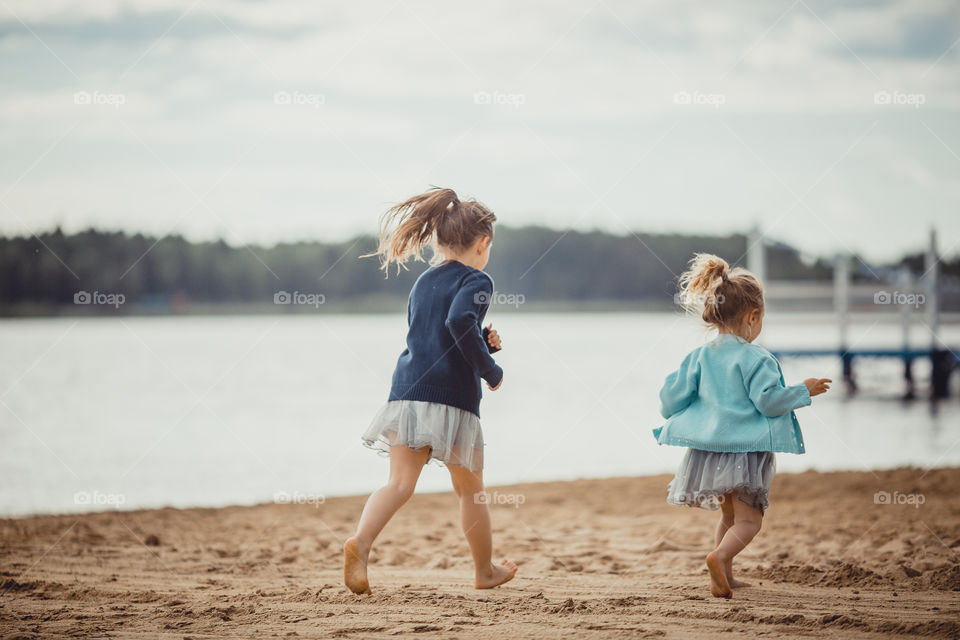 Little sisters on lake coast at sunny evening. 