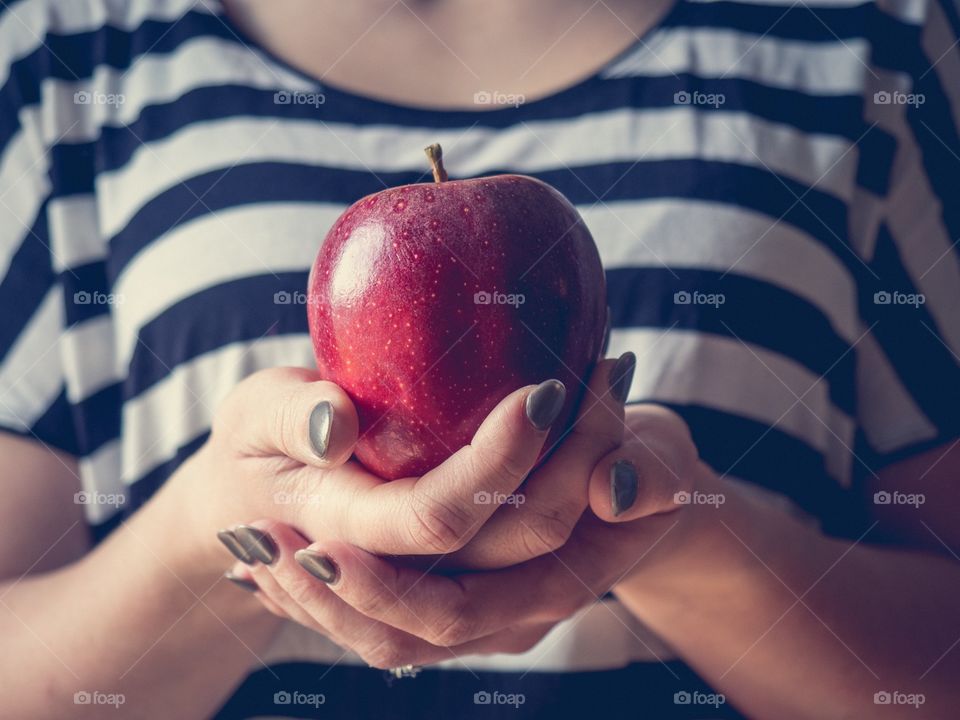 Two hands cupped under an apple with a matte finish