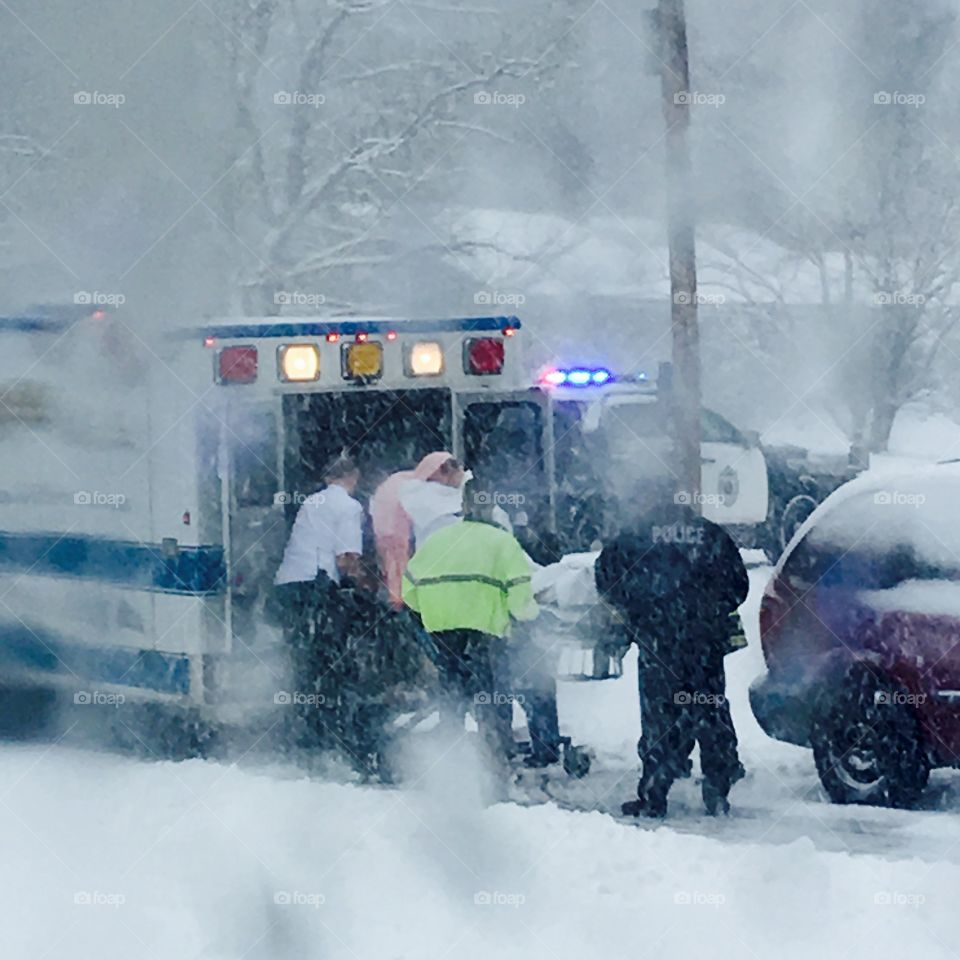 Ambulance, Emergency Ride To Hospital
Police & EMT lifting patient up into back of ambulance. Doors are wide open and in they go! Police car siren is making a howling noise as the blizzard goes on. Lights are flashing, they are in a hurry & I see one man has no coat on. It's freezing out. It is an emergency!