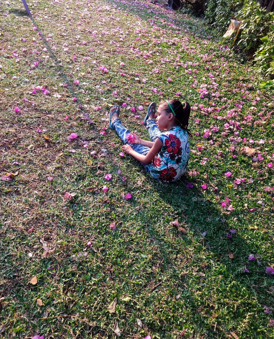 Captivating childhood essence of simply finding joy of toy in anything around them. Adorable Baby girl emersed in playing with vibrant pink flower, bathing in soft glow of dusk light making earth her playground unbothered.