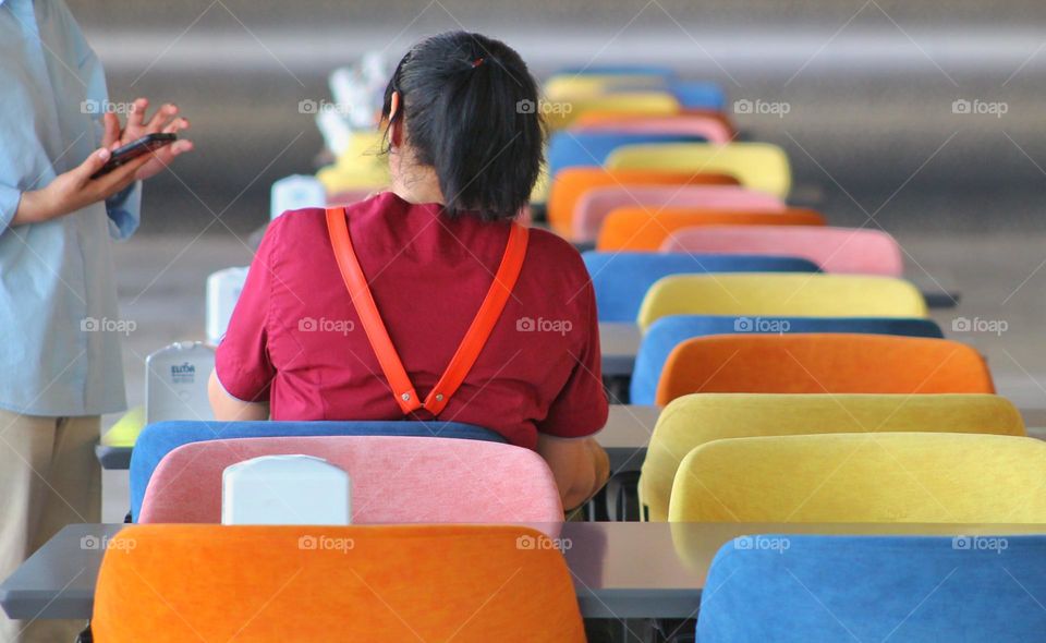 a waiter in a cafe takes an order from a girl in a red T-shirt. Really stylish multi-colored chairs lined up.