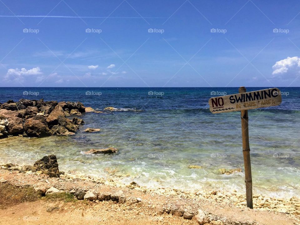 Beautiful landscape view from the rocky sand shore over the Caribbean sea with No swimming sign