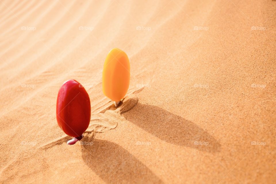 Two colorful ice cream melting in hot sand, dessert in desert 