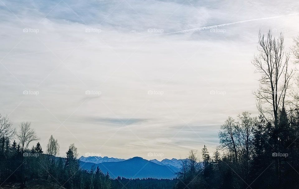 Landscape photography with black silhouettes of trees blue shapes of a mountainscape and e light cloudy sky