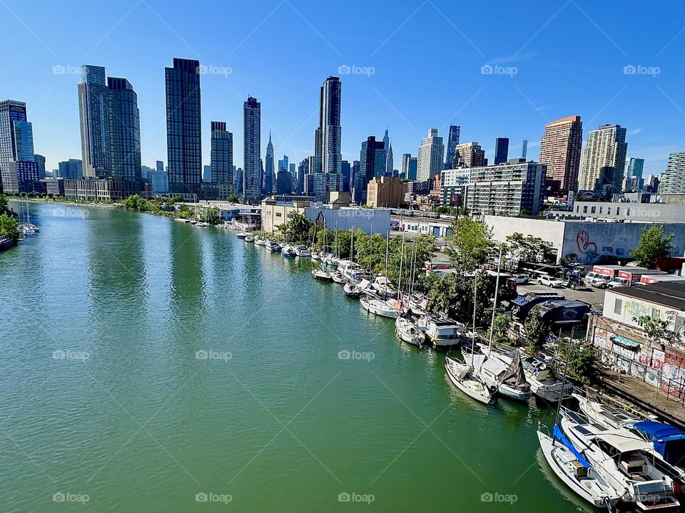 This is “Newtown Creek”, ocean inlet of the “E River” w its great variety of boats seen from the “Pulaski Bridge” that connects “Greenpoint”, Bklyn to LIC. In the distance we see “Manhattan” incl. the “Empire State Bldg”. 2024. Hypnotic Productions
