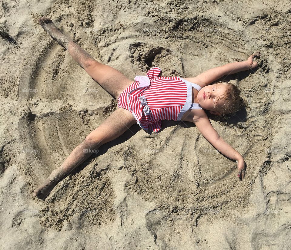 Elevated view of girl making sand butterfly