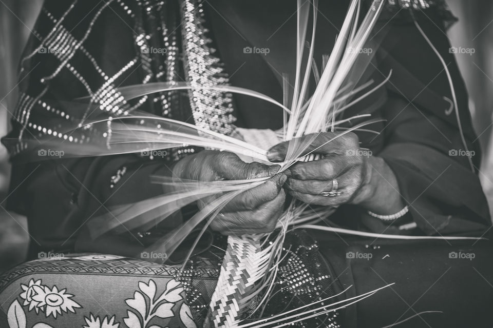 Woman weaving basket from dry palm leaves, hands in frame