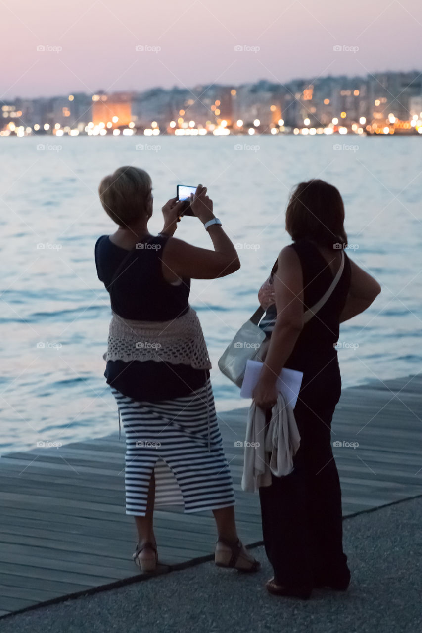 Middle-Aged Woman With Her Friend Photographing A Cityscape With Smartphone
