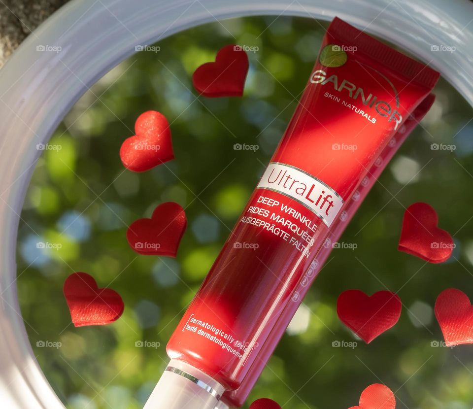 Garnier Skin Naturals Ultra Lift, displayed on a mirror reflecting a blurred green leafy background and surrounded by hearts