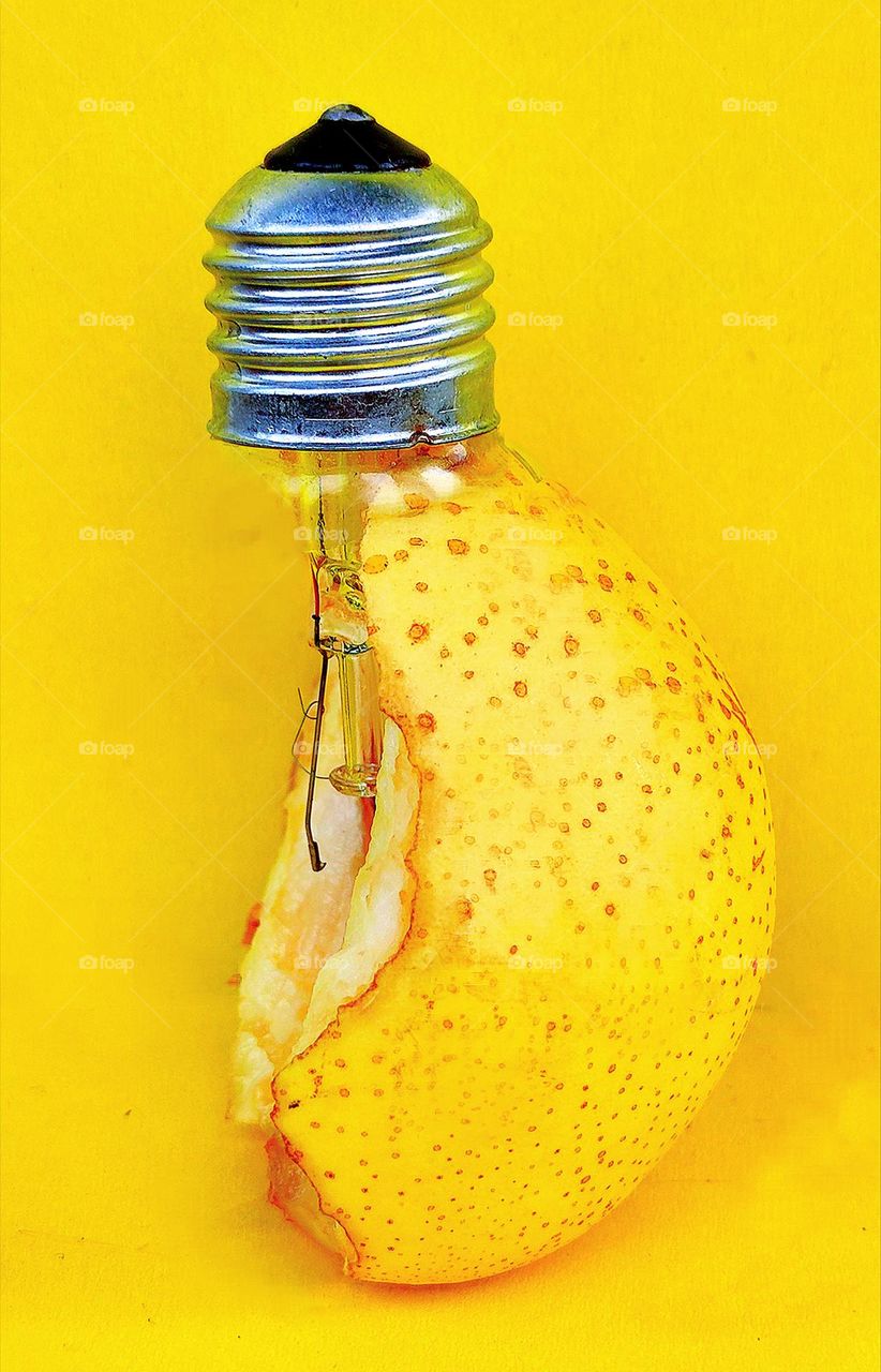 Fruit. On a yellow background is a yellow bitten off pear, into which a light bulb is inserted. The similarity of the shape of a light bulb and a pear