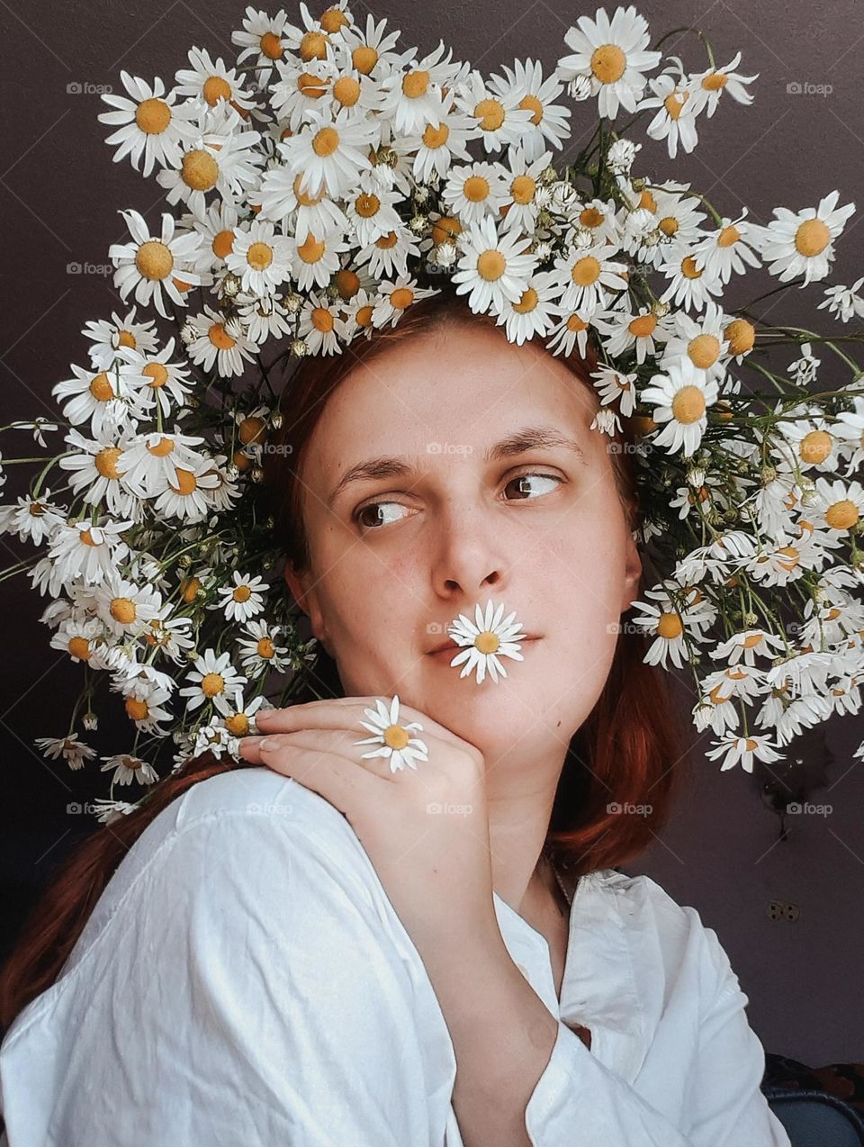 an original portrait of a girl with flowers on her head, namely a wreath of field daisies and looking away