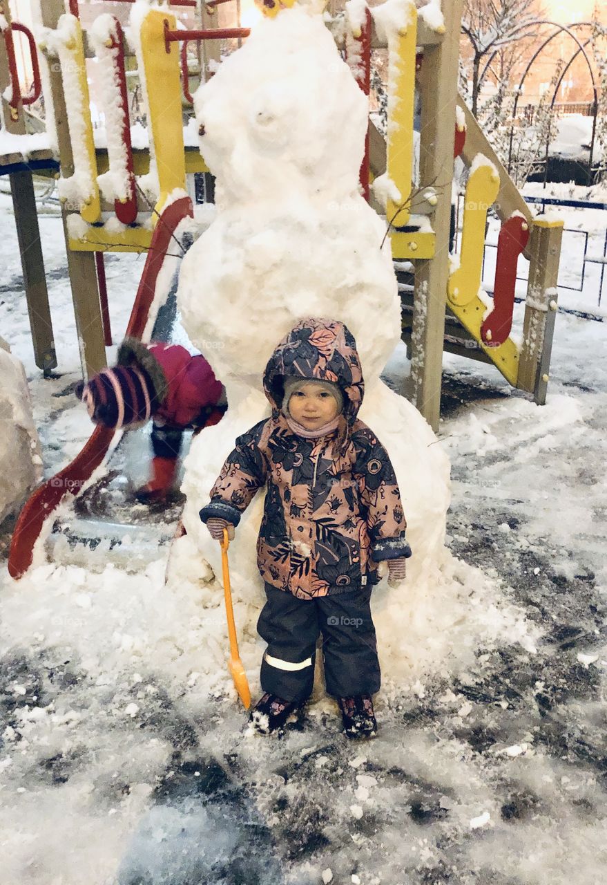little girl in winter overalls walks and plays snowballs
