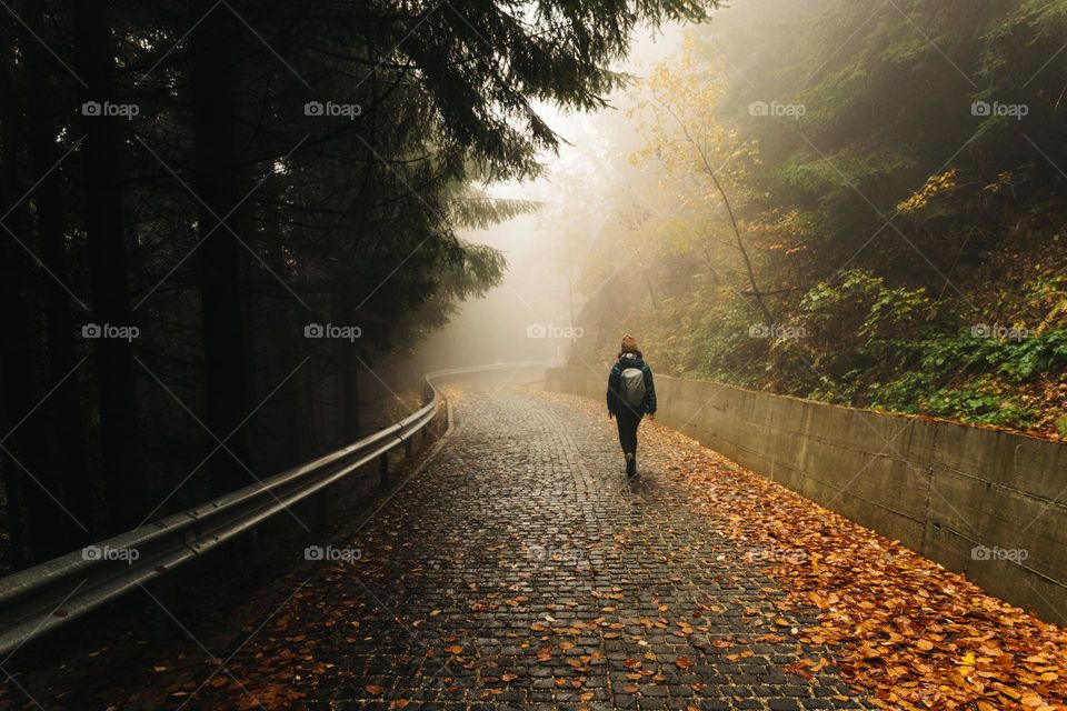 Woman walking on an empty road, on a foggy autumn day.