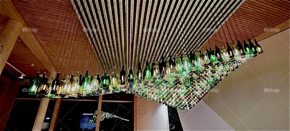 This is the suspended bottle light installation at „Navareum“, a concert hall venture in the beautiful city of „Straubing“, „Bavaria“, Germany. Each bottle is individually illuminated and the light show changes over time. 2023. Hypnotic Productions