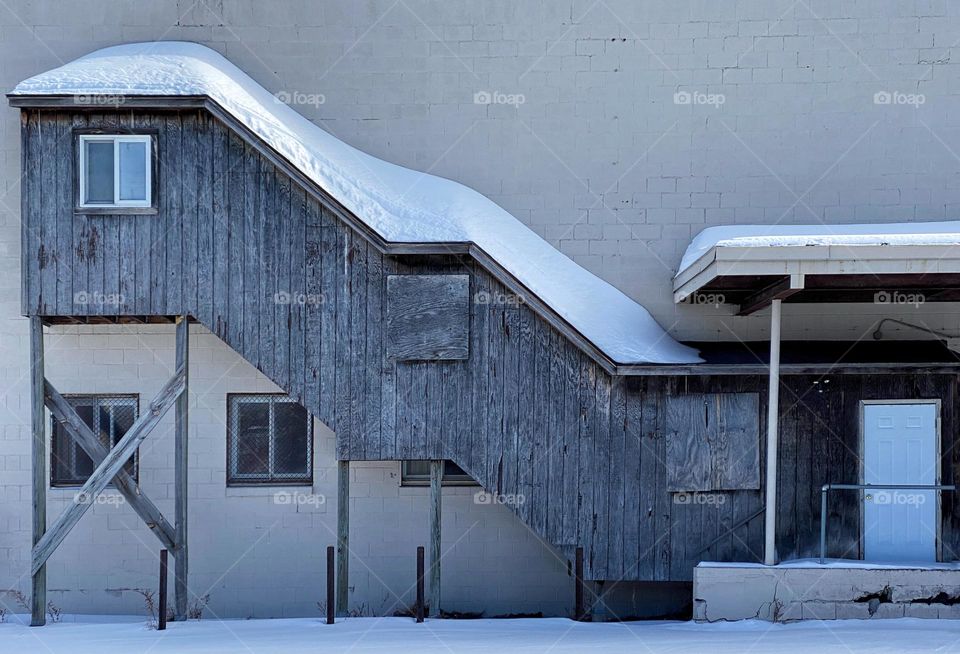 An enclosed staircase on the outside of a factory building with snow on the roof