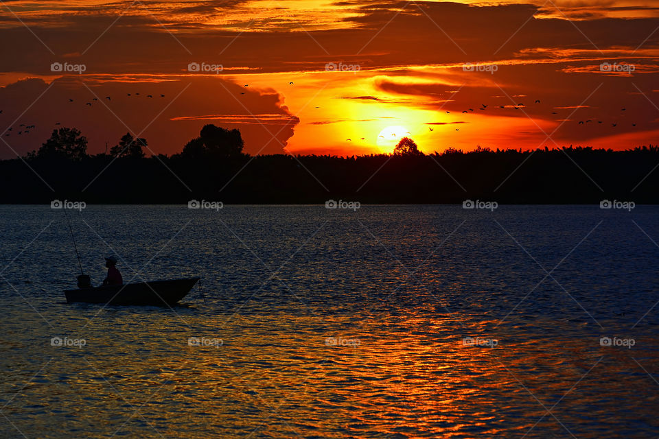 A fishing sunset. A lonely man with his boat fishing at sunset