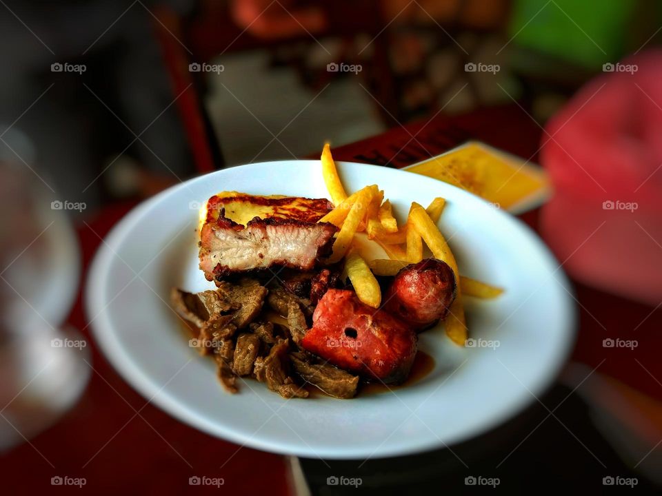 a barbecue many people like, here is a plate with meat, sausage and french fries.