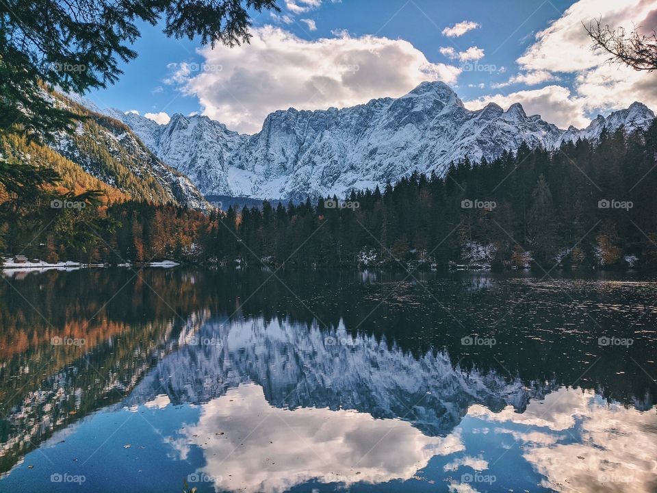 View of the autumn snow-capped mountain peaks against the backdrop of a transparent Italian lake.