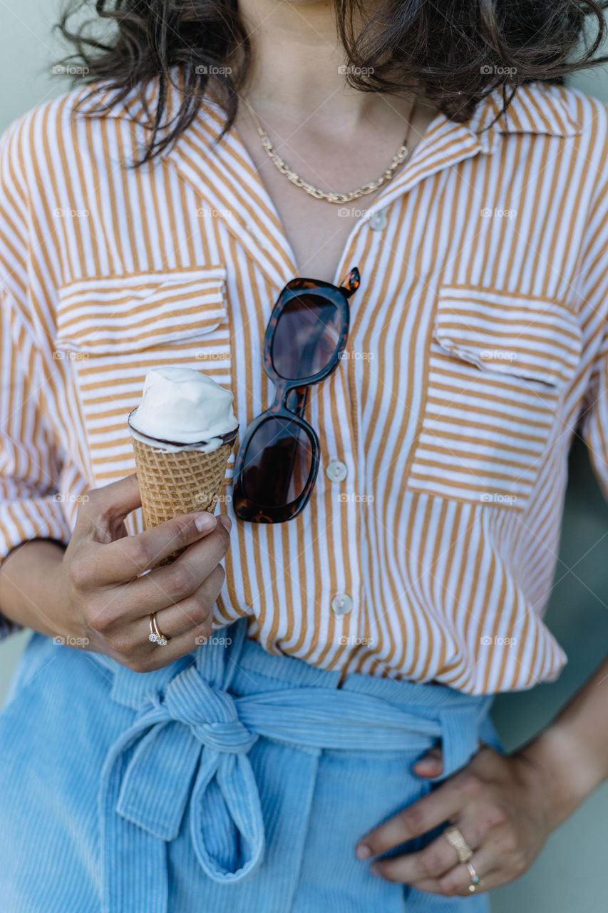 Woman wearing gold jewelry while eating icecream on a hot summer day.