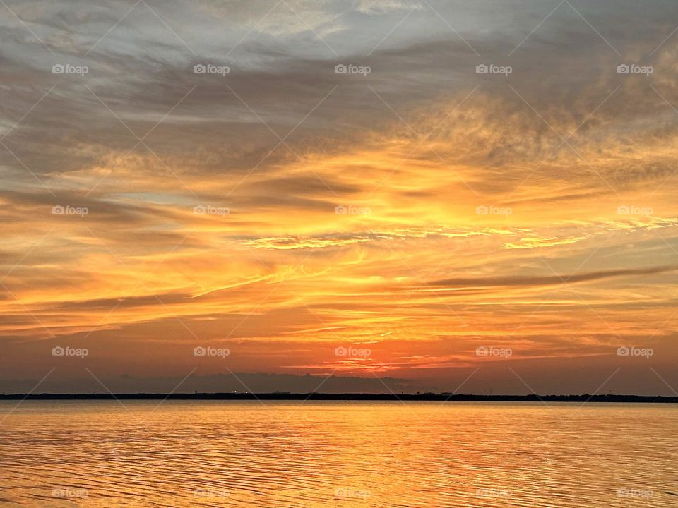 The glowing, descending setting sun gave a warm orange tinge to the sky and cast an iridescent shadow on the waters surface