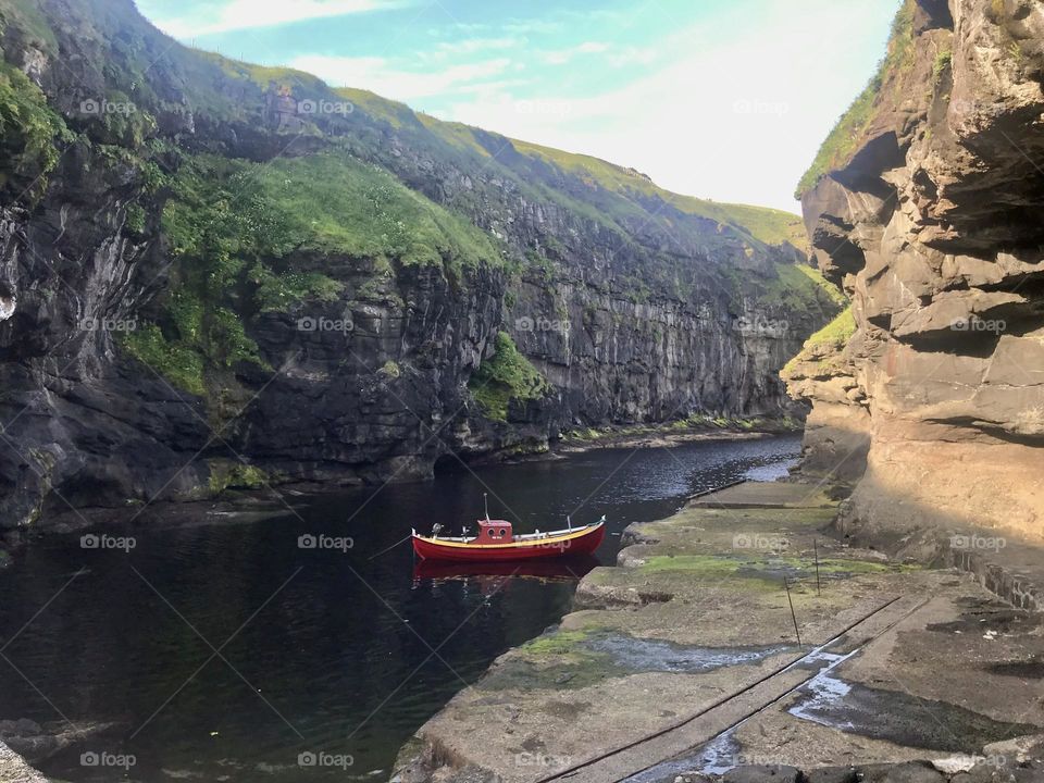 Small colorful fishing boat in tiny cove surrounded by green rocks in the Faroe Islands 