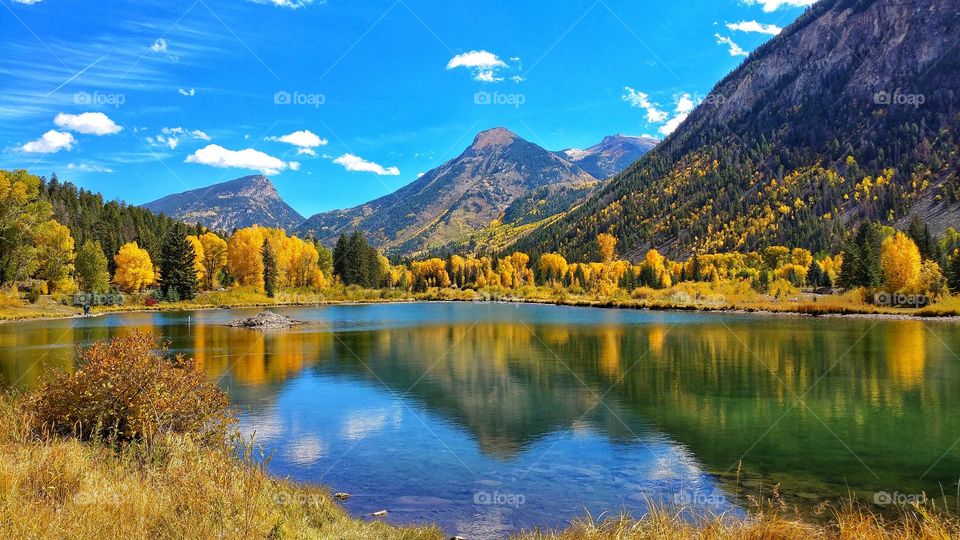 A vibrant blue sky reflects on a high mountain lake surrounded by golden autumn leaves.