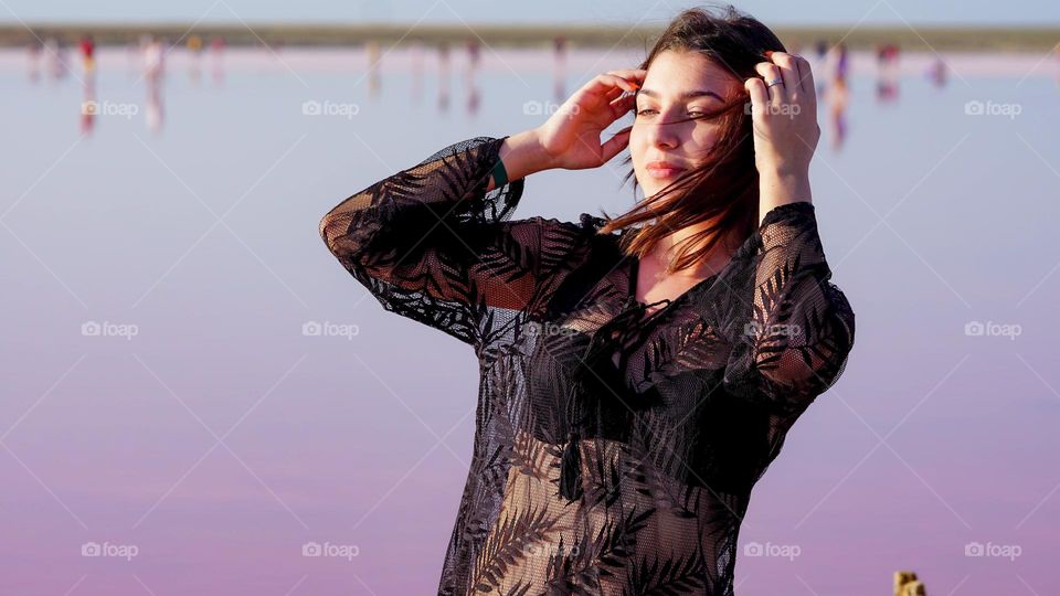 An young brunette girl against pink lake surface, summer time, windy day 