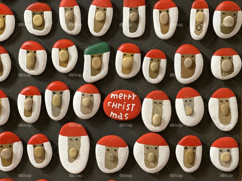 Many handmade stone Santa Claus magnets on a wooden board 