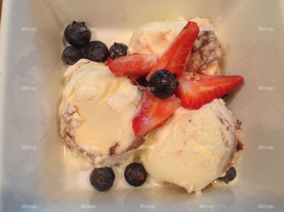 A photo of Vanilla ice cream with strawberries and blueberries. 