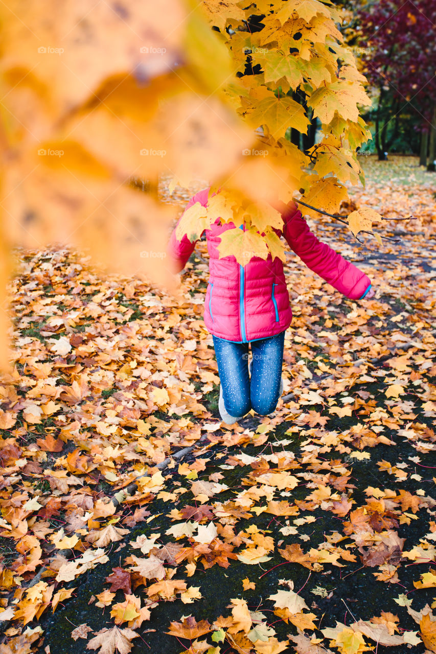 Girl jumping behind branch with yellow autumn leaves in a park