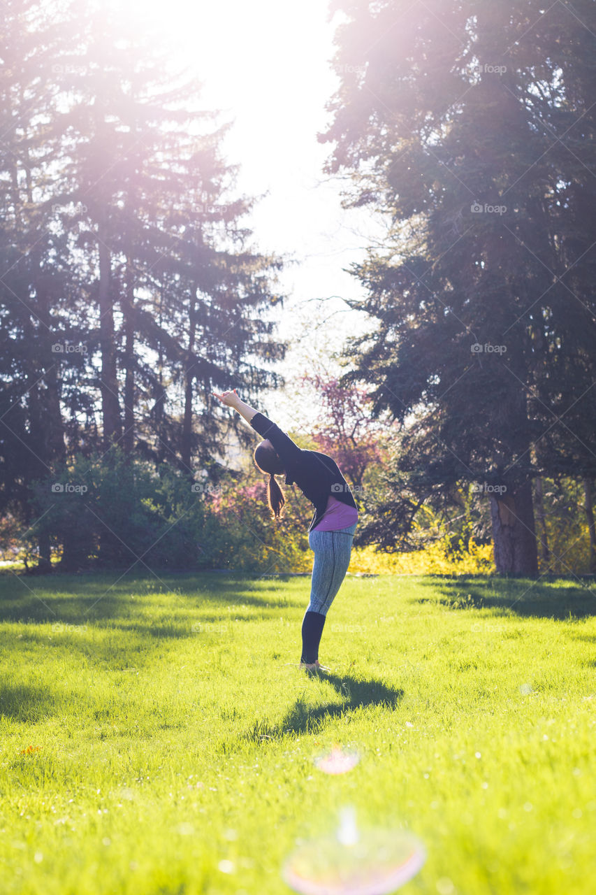 A yoga teacher practices tree poses in the middle of a field during spring as golden hour starts and she glows connected to nature 