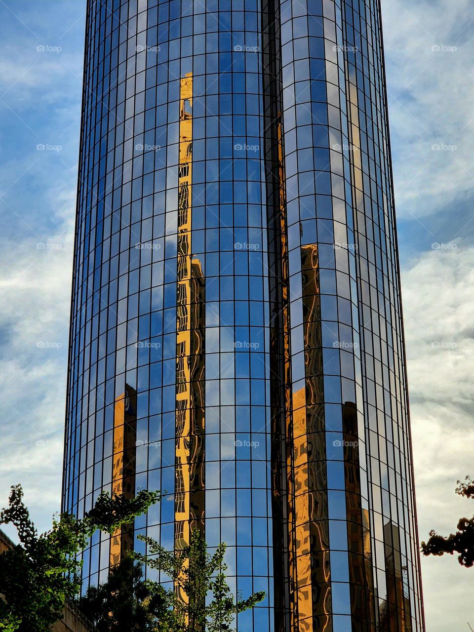A nearby building is reflected on the side of a tall round glass building providing a unique perspective