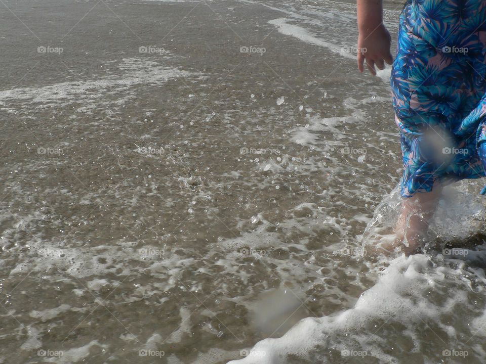 Glimmer moment at the beach with a girl child dressed with blue leaves flowers motifs designed on modest swim dress suit with the young girl walking and enjoying the shore and loving the waves and warm ocean water.