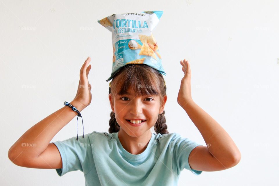 Cute happy girl balancing bag of chips on her head