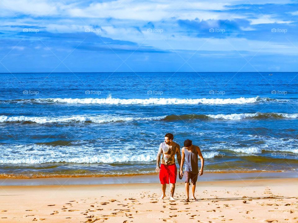 Two men walking on the beach, at sunrise, with a Beautiful Blue sky and ocean waters behind them.
Tattooed men and his friend pn a Summer holiday tropical vacation.