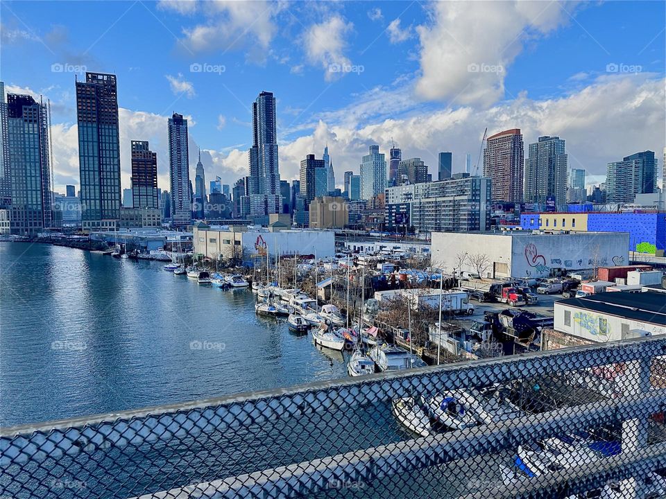 This is the view from the “Pulaski Bridge” that connects LIC, Queens and “Greenpoint”, Bklyn overlooking “Newtown Creek” and its many boats of all sorts. In the distance there is “Manhattan” incl. the “Empire State Bldg”. 2023. Hypnotic Productions