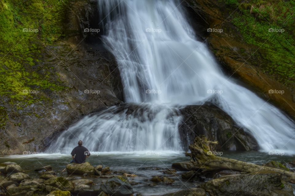 Rear view of person sitting against waterfall