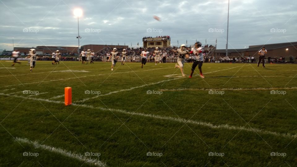 High school football receiver dives for a pass in the end zone of a varsity contest on a football Friday night.